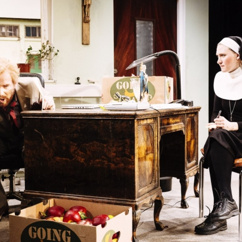 En man talar i telefon medan en nunna sitter på en stol