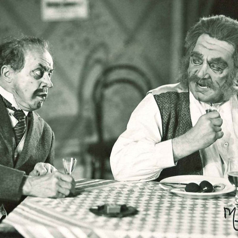 två män sitter vid ett bord med rutig duk