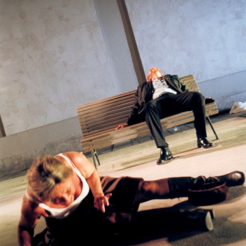Kvinna tar sig upp från golvet och en man sitter på en bänk