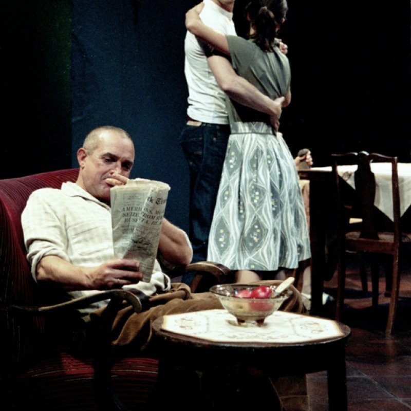 En man läser tidningen medan en man och en kvinna kramas