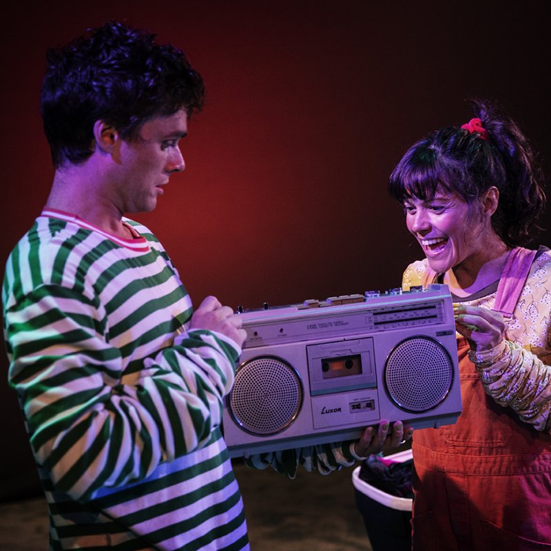 Två personer håller en kassettebandspelare mellan händerna och de tittar glada på den. 