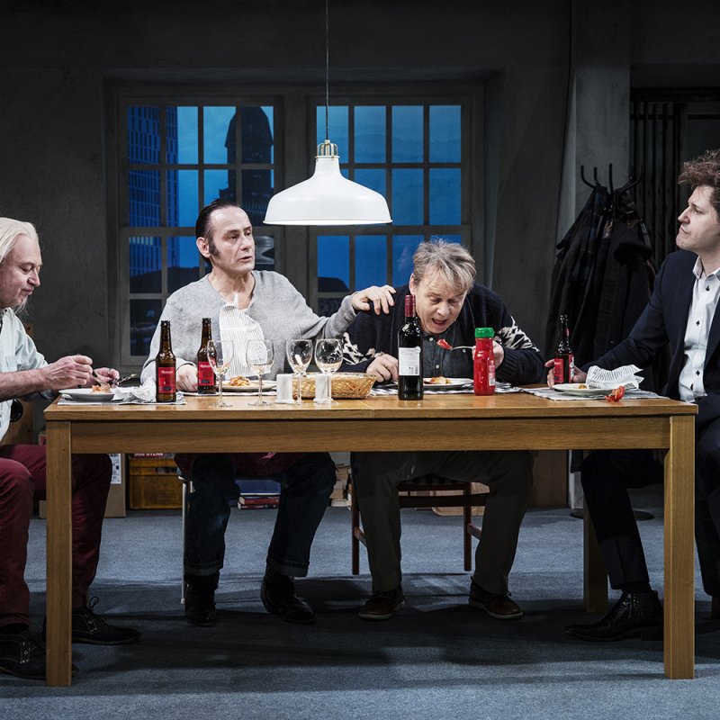 De fyra medlemmarna sitter kring ett matbord och äter lasagne. 