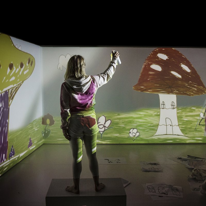 Flicka står i ett rum med stora svampar tecknande på väggarna