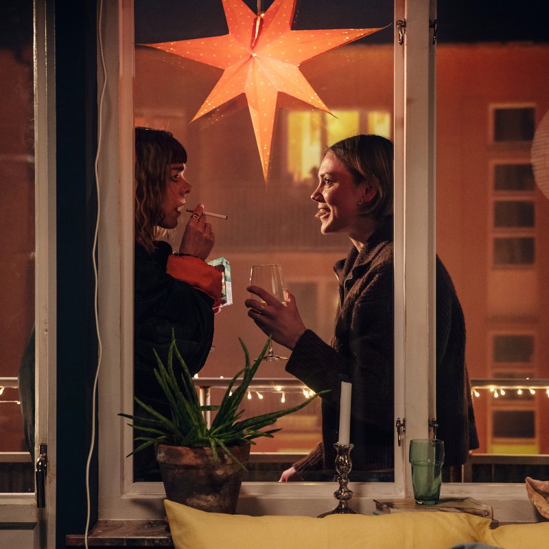 Två personer pratar på en balkong. Julstjärna i fönstret.
