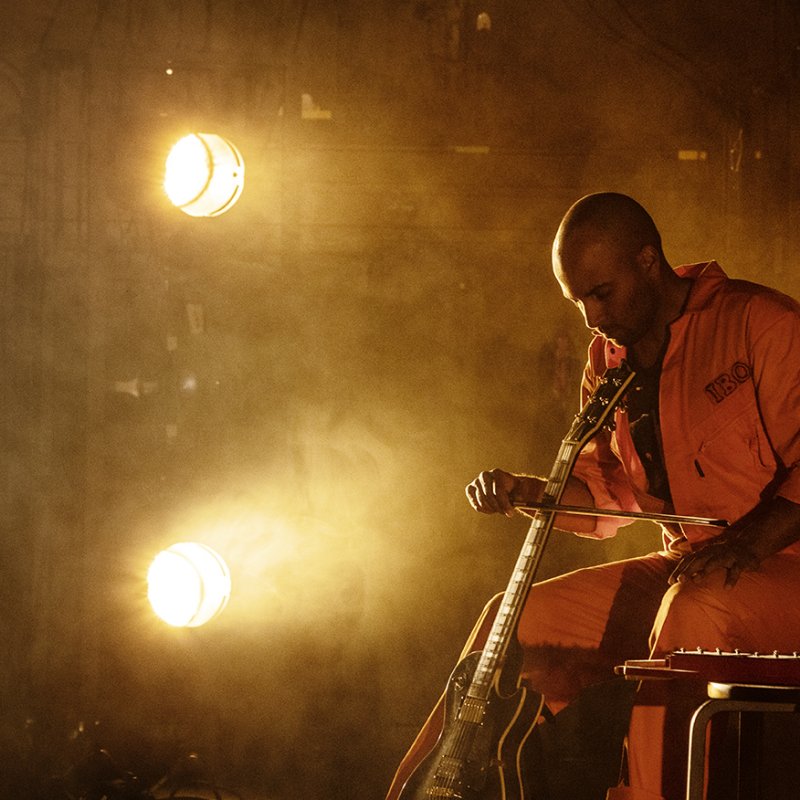 En man i orange overall spelar på gitarr
