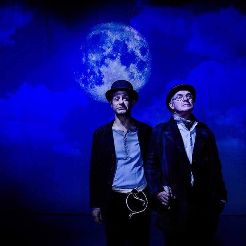 Estragon och Vladimir står med en kvällshimmel med måne i bakgrunden.