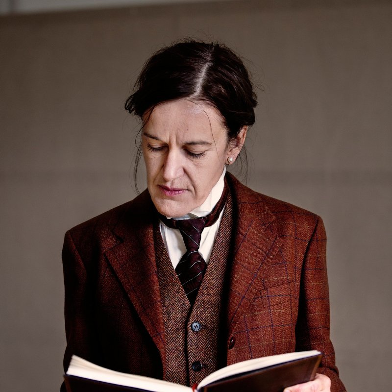 Kvinna i strikt kostym av äldre snitt läser i en bok.