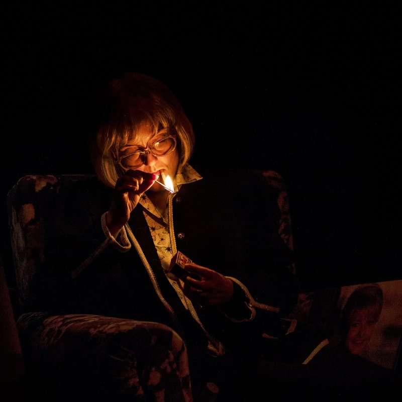 En gammal Monica tänder en cigarett i mörkret