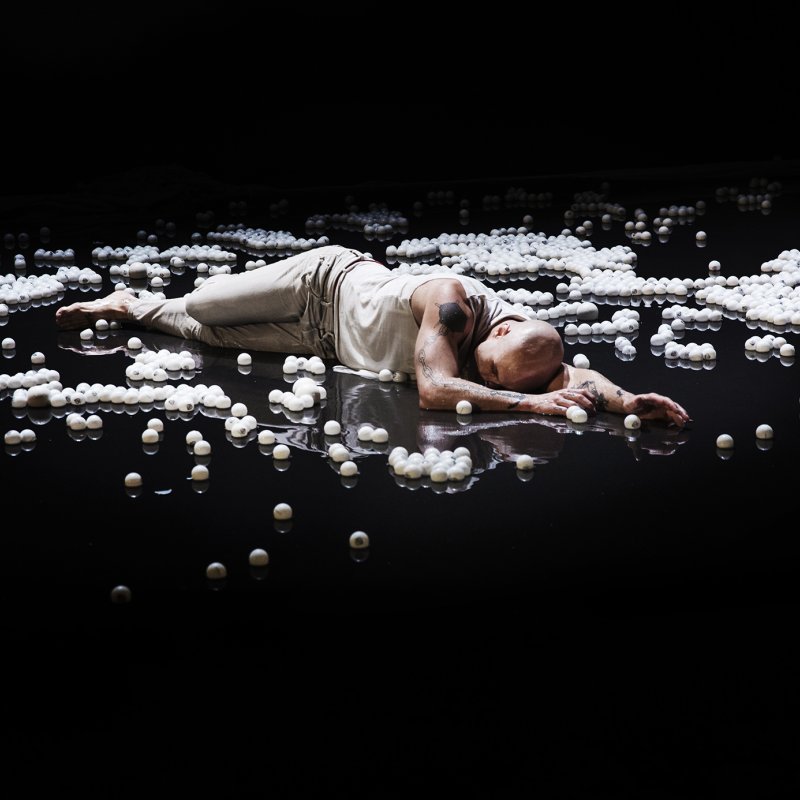 En man ligger i ett hav av flytande vita bollar.