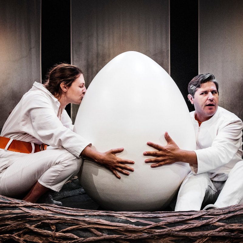Två personer kramar ett stort ägg i ett fågelbo.