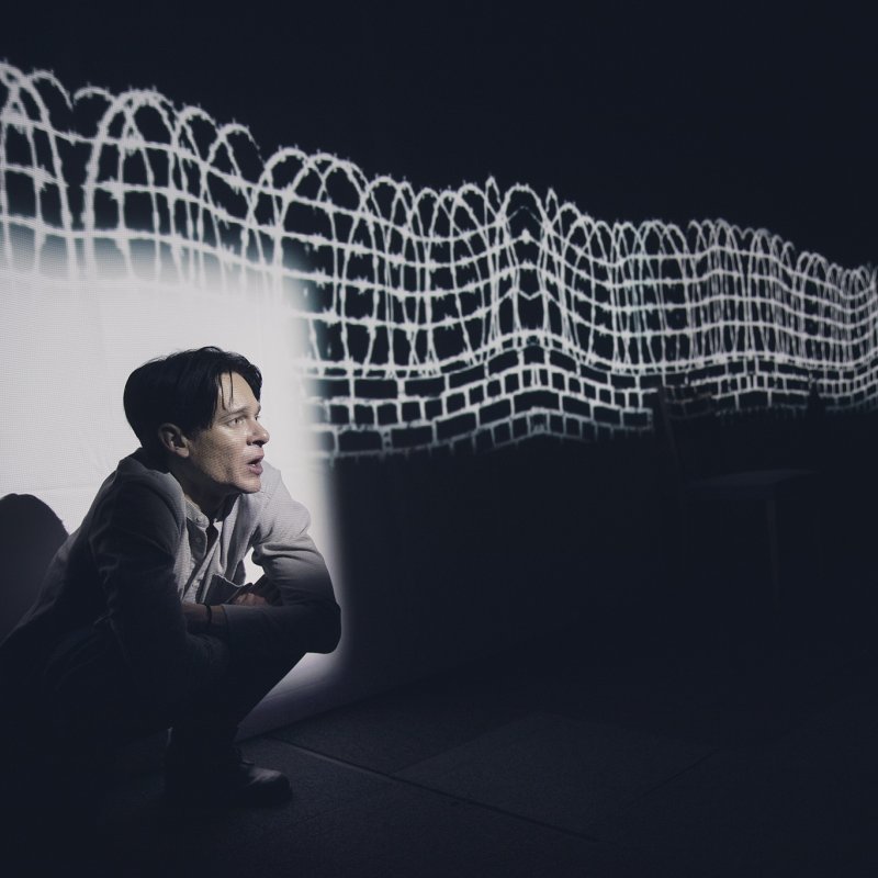 Person sitter vid en projection som visar en mur av taggtråd