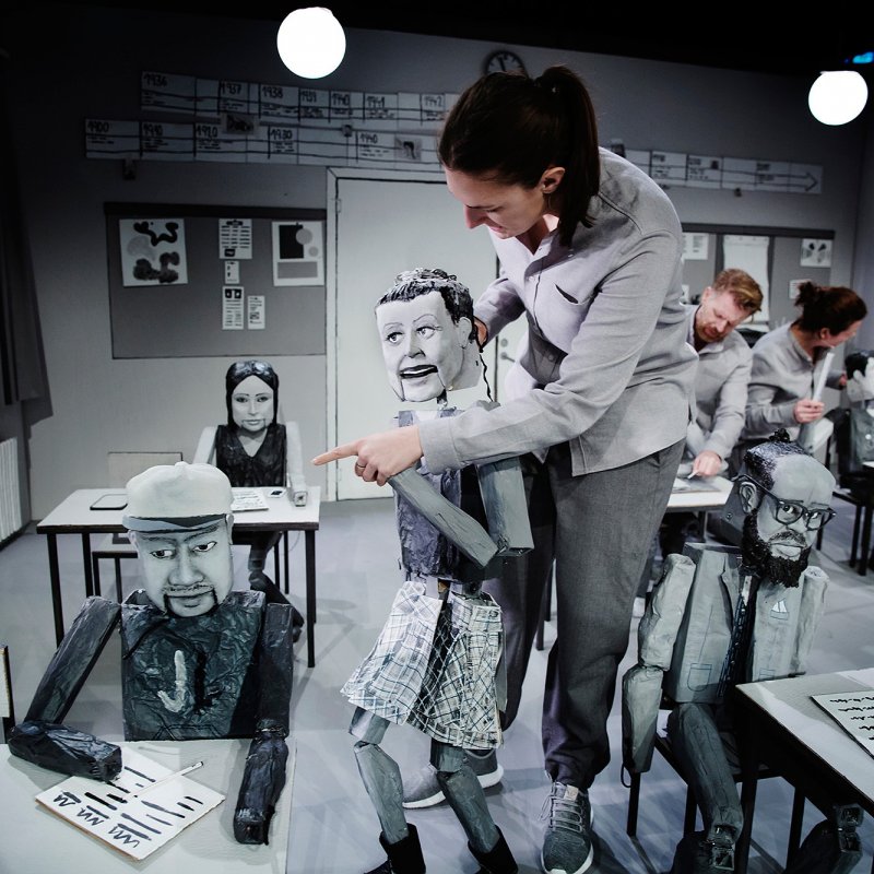 Skådespelare går omkring med en docka i klassrummet som pekar på en elevdocka.