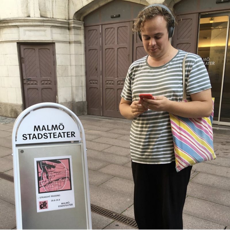En man står med telefonen och ett par hörlurar utanför Hipps entré  redo att börja sin vandring runt Malmö.