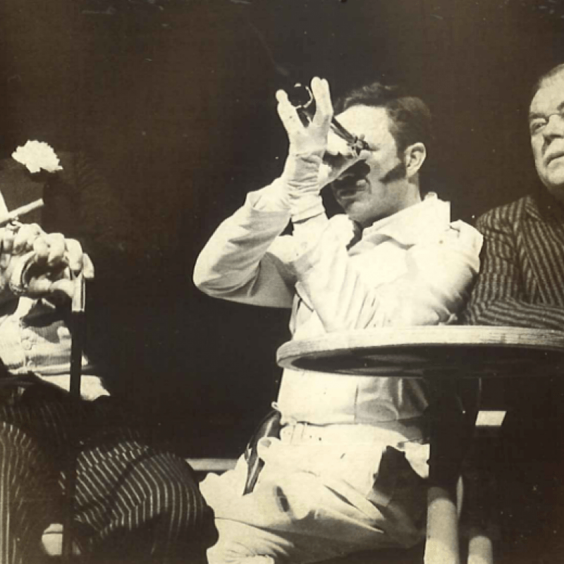 Tre män vid bord, en med kikare