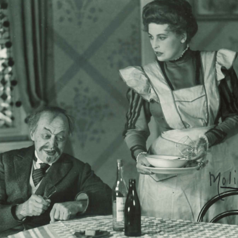 man dricker vin vid bord och kvinna står bredvid