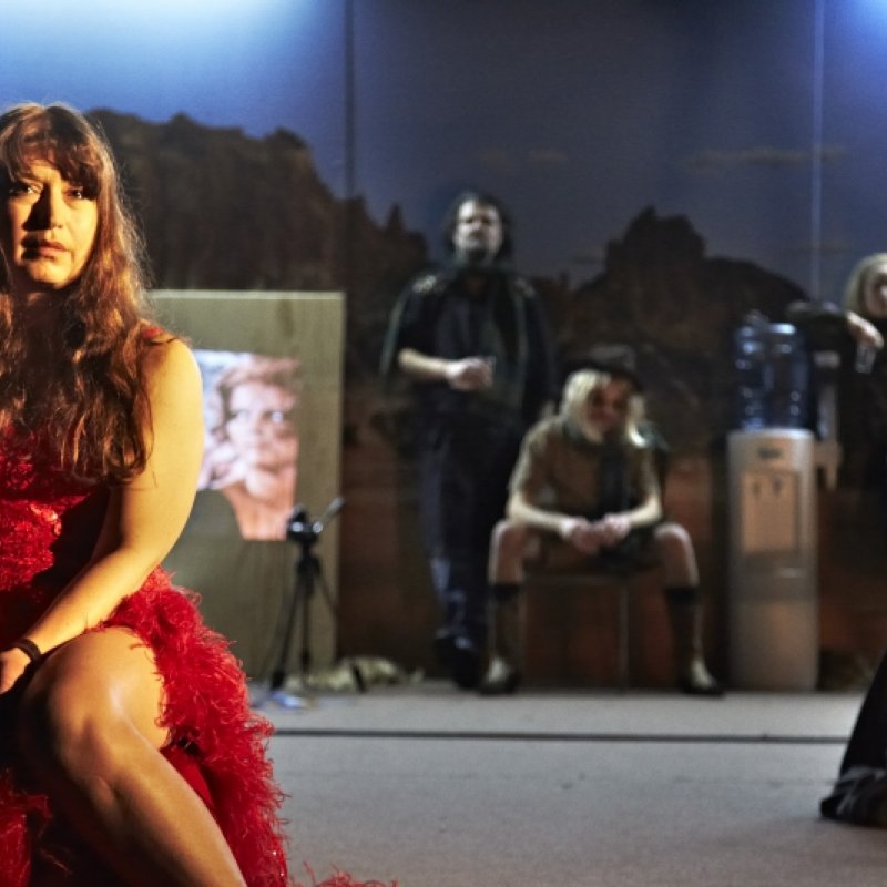 En kvinna i röd klänning sitter i förgrunden och tre personer syns i bakgrunden