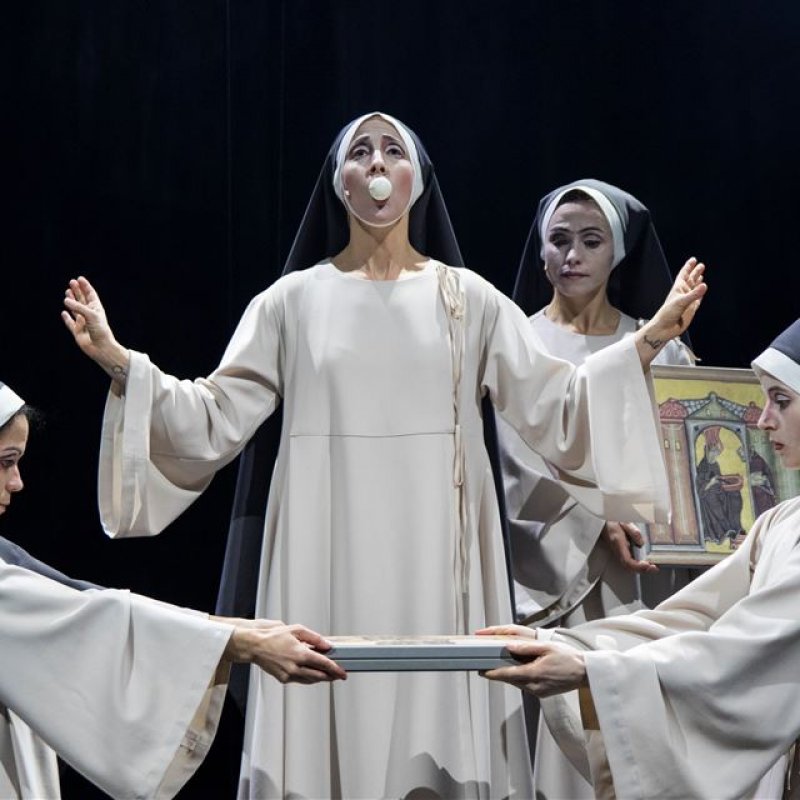 Två nunnor i förgrunden håller två plattor mellan sig. En annan nunna har en pingisboll i munnen och ytterligare en håller i en tavla