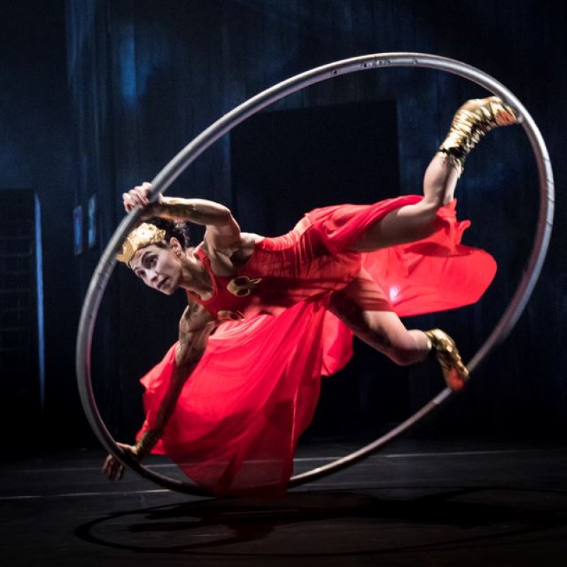 Kvinna i röd klänning och guldaccessoarer utför cirkuskonster i en stor ring på golvet