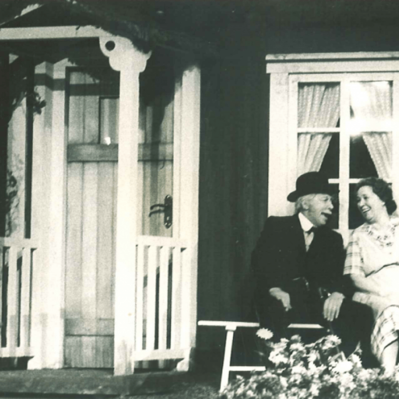 En man och en kvinnan sitter på en bänk utanför en stuga