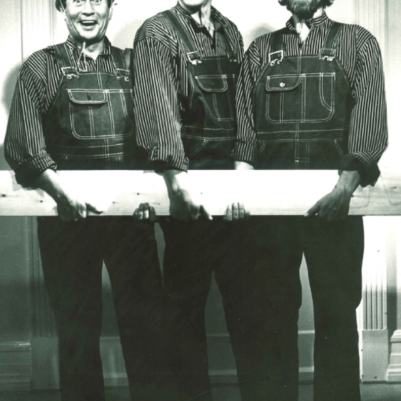 Tre män bär en planka