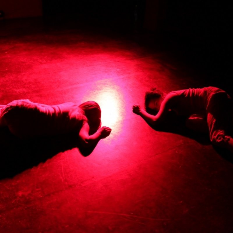 Två personer ligger på scenen i rött ljus