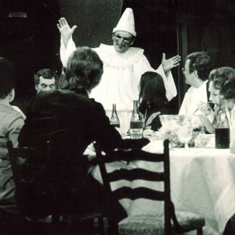 En samling runt ett bord och en vitklädd man som gestikulerar