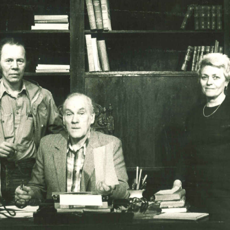 Tre personer. En sitter och de övriga två står bakom ett skrivbord