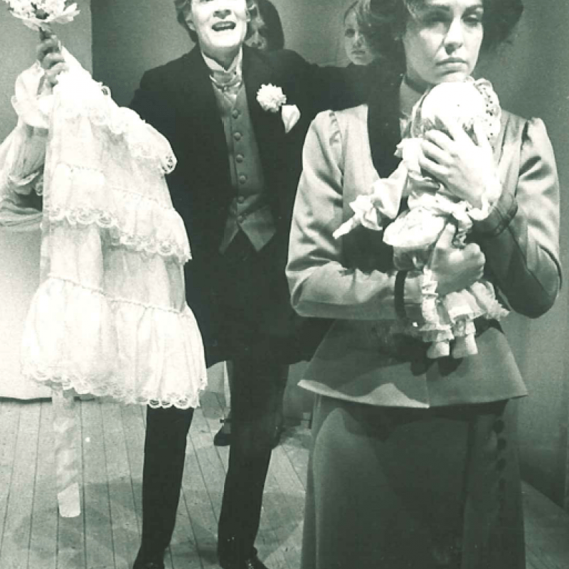 Kvinna kramar docka medan en man står bakom henne med en bröllopsklänning
