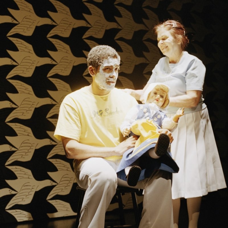 Två personer med vitmålade ansikten tar hand om en docka