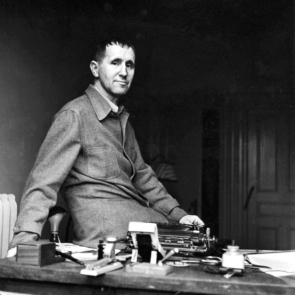 Bertolt Brecht sitter på ett skrivbord och tittar in i kameran
