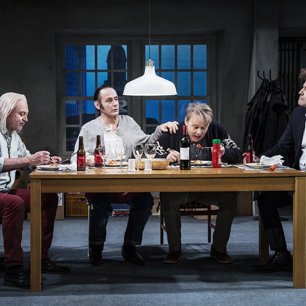 Fyra män sitter kring ett bord och äter lasagne och dricker öl.