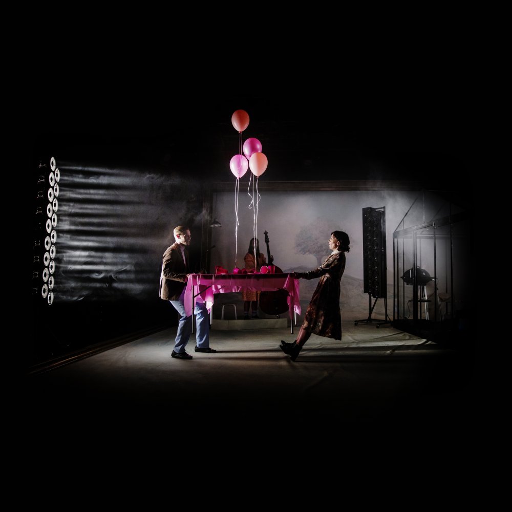 två skådespelare lyfter ett bord som har gas-ballonger fäst i sig