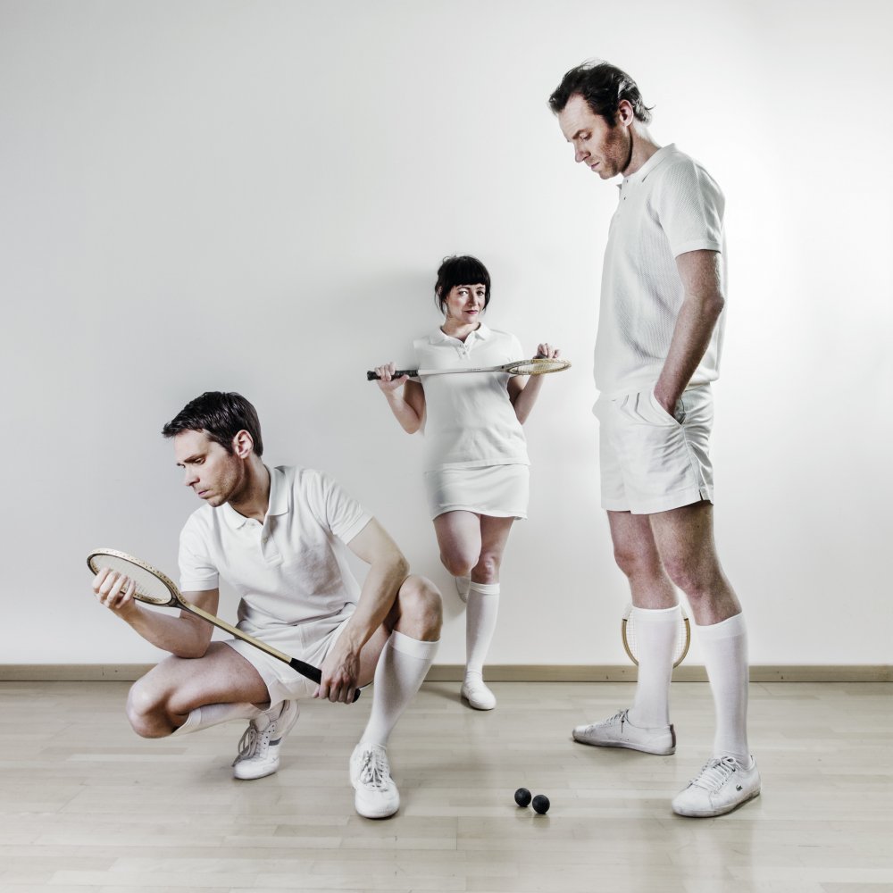 Ensemblen poserar iförda vita sportkläder hållandes squashrakettar Foto: Emmalisa Pauly